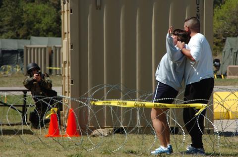 A sailor simulating a crazed husband holds a gun on his wife during a training exercise
